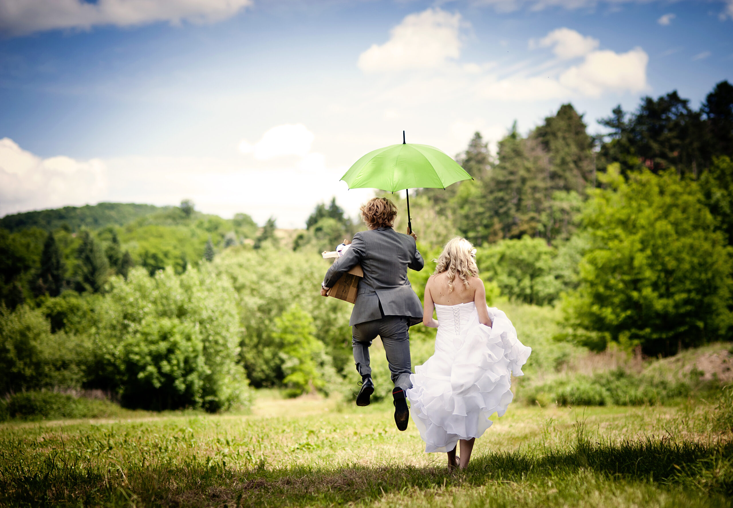 bride and groom running through field with umbrella